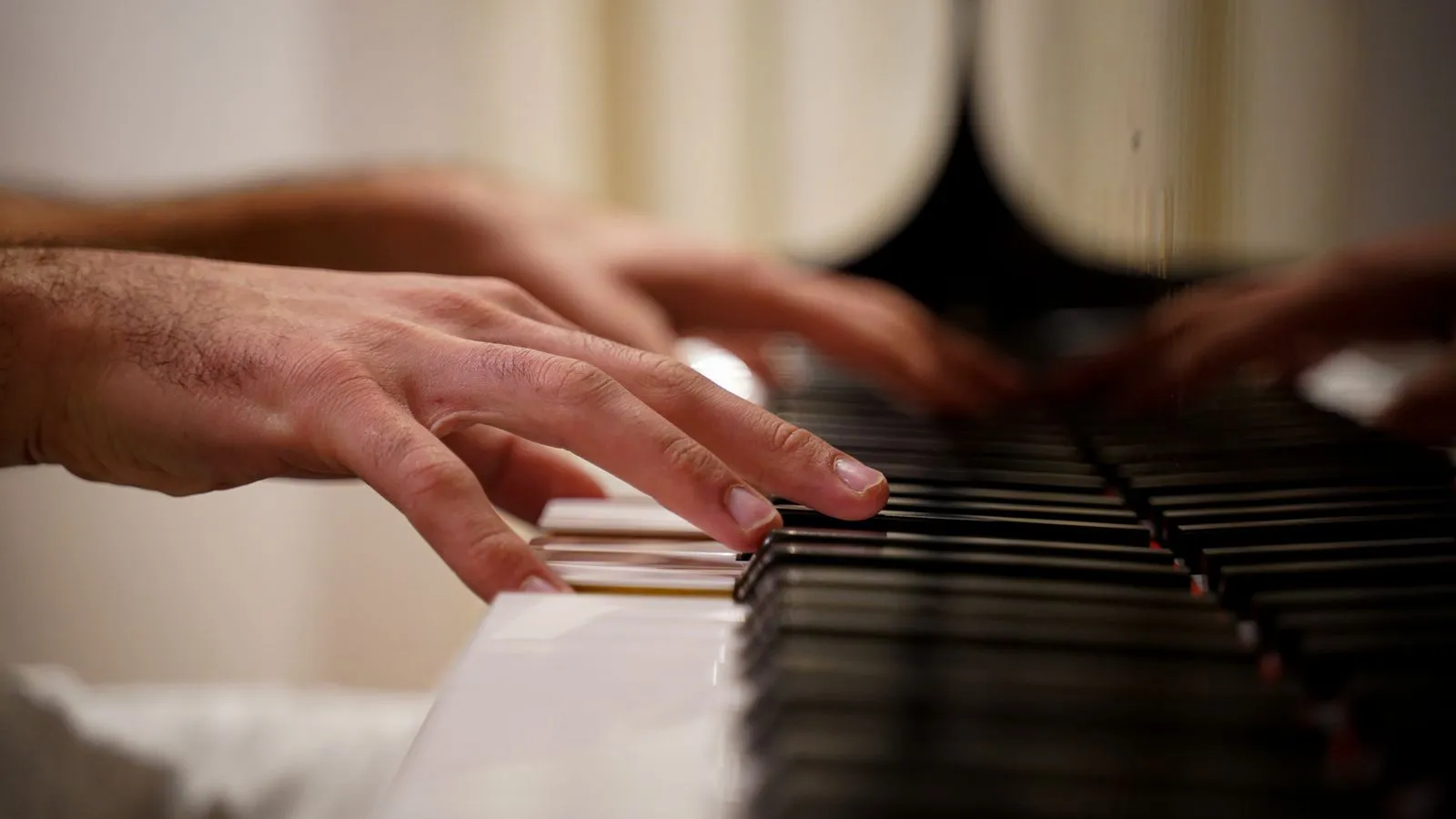 Focused view of hands playing piano keys indoors with reflection visible.
